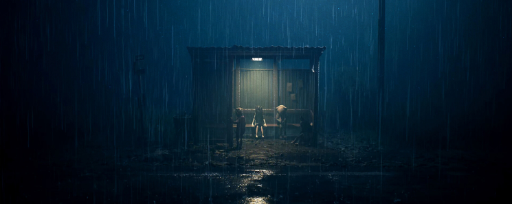 Dos figuras de pie bajo la lluvia junto a un cobertizo iluminado